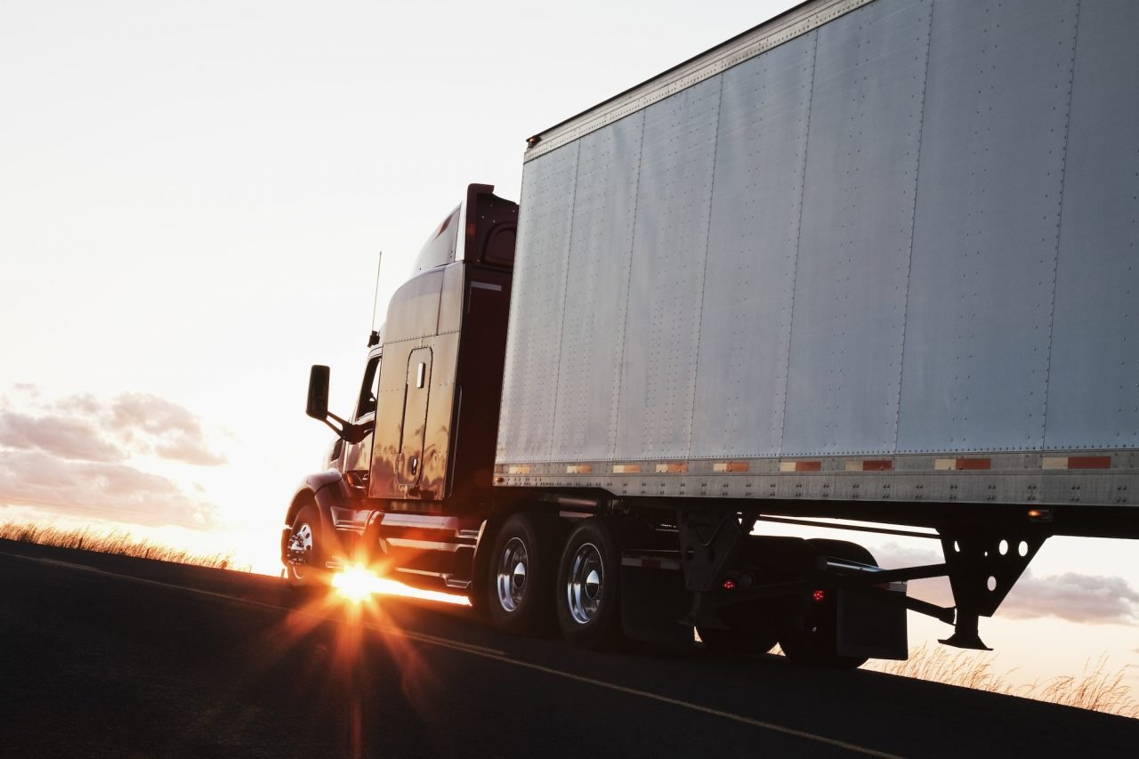 silhouette of a commercial truck driving on a highway at sunset .jpg